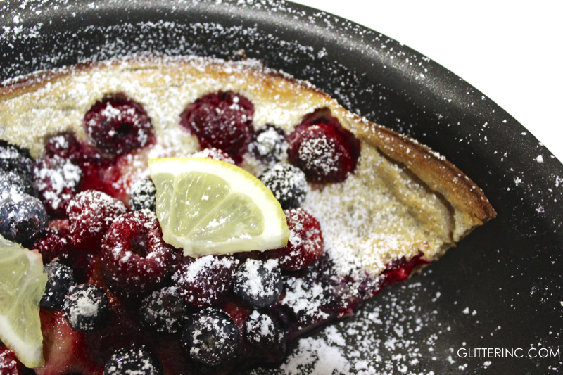 dutch baby pancake with powdered sugar lemon raspberries and blueberries - recipe - glitterinc.com