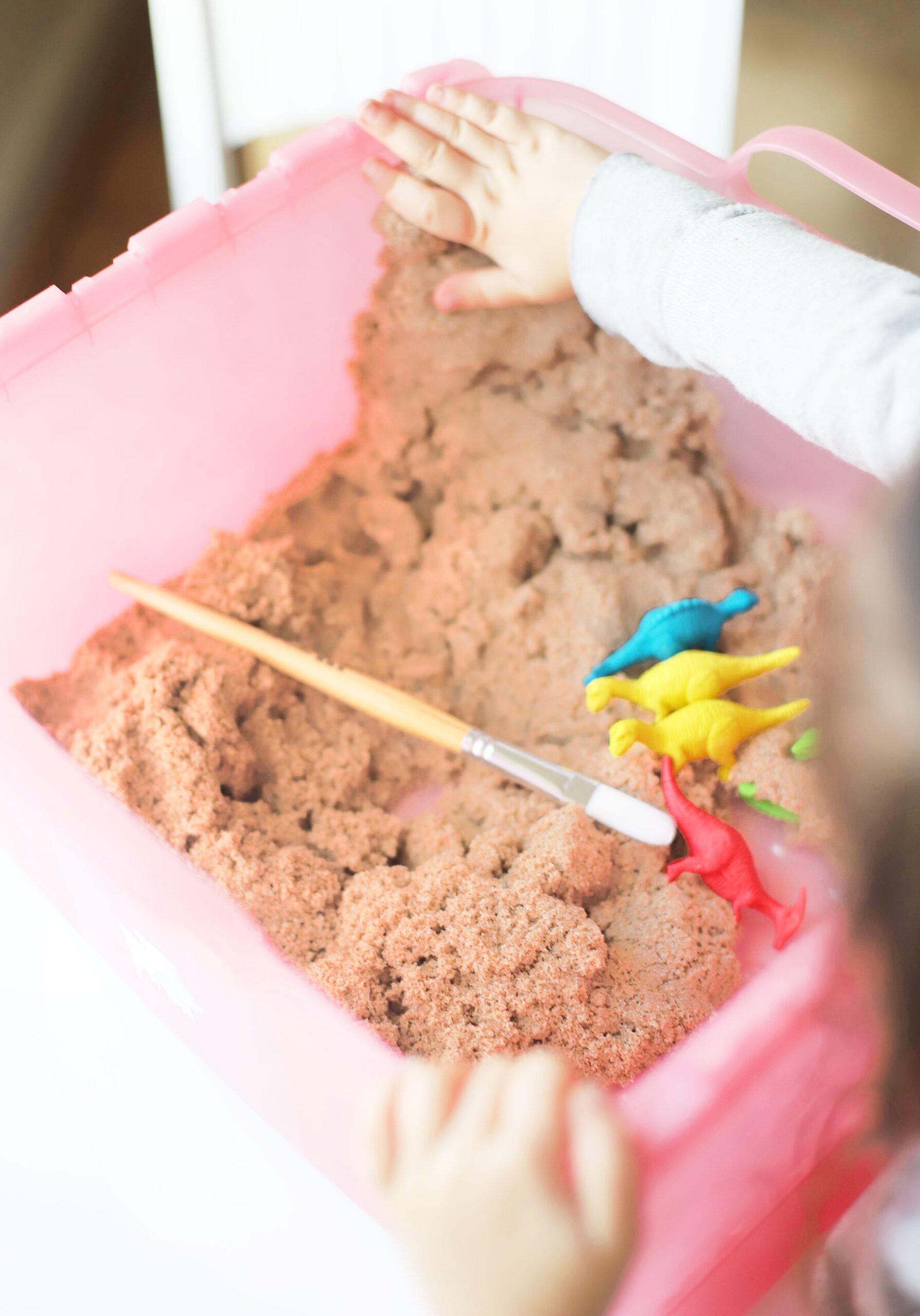 Home with your young kids? Here is a huge list of fun and educational activities to do at home with young kids, including exactly how to entertain your children during school closures, cold and flu days, Spring and Summer vacation breaks, and more. | glitterinc.com | @glitterinc // Create your own DIY kinetic sand dinosaur dig. This kids activity is an awesome, mostly mess-free way to dig into sensory play, all in one convenient bin.