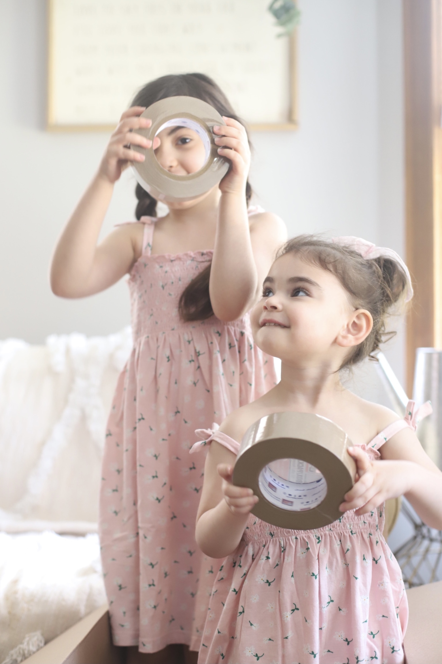 two kids wearing pink dresses and holding packing tapes to show We Bought a House post