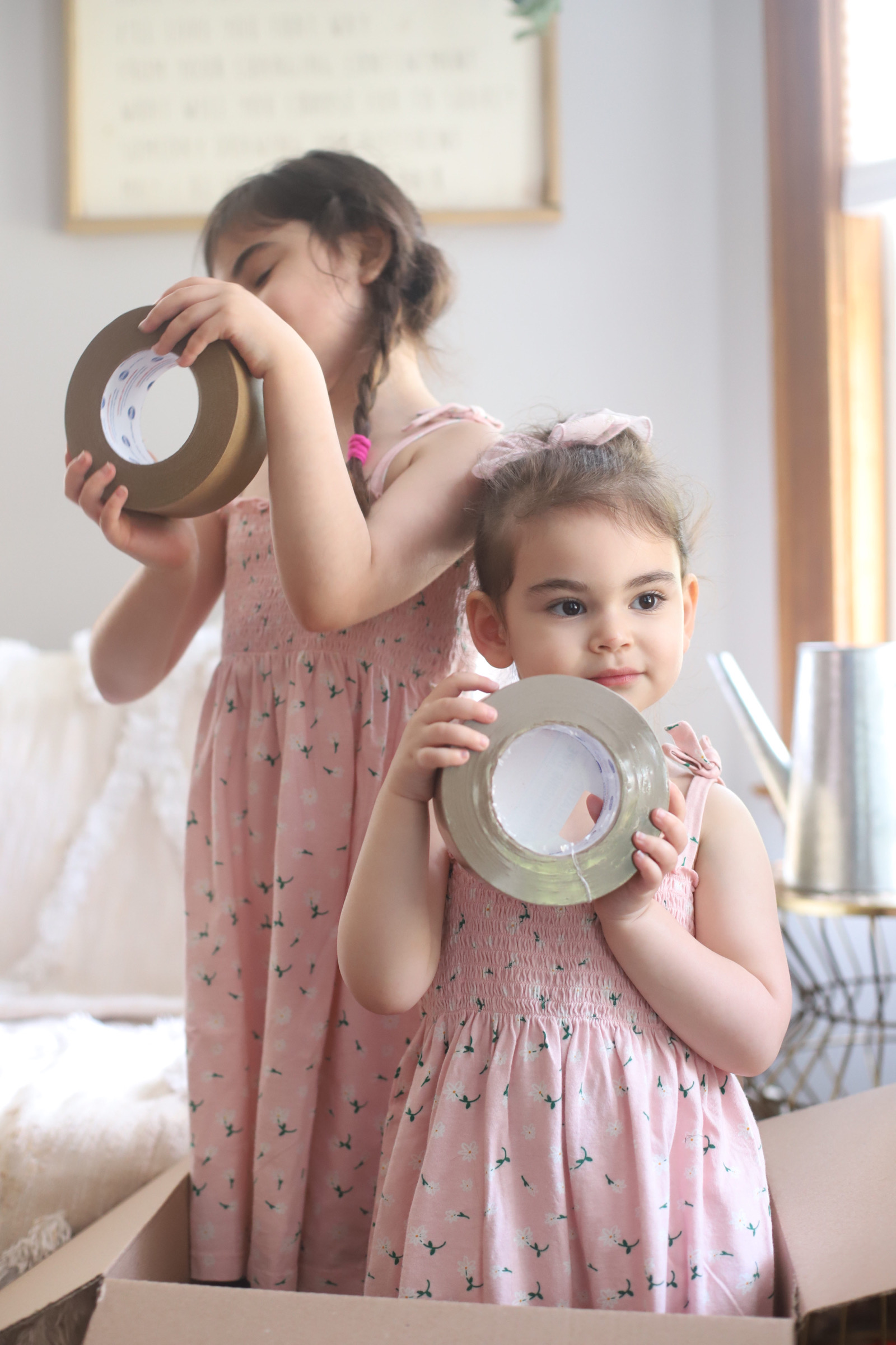 two girls wearing pink identical dress and playing with packing tapes