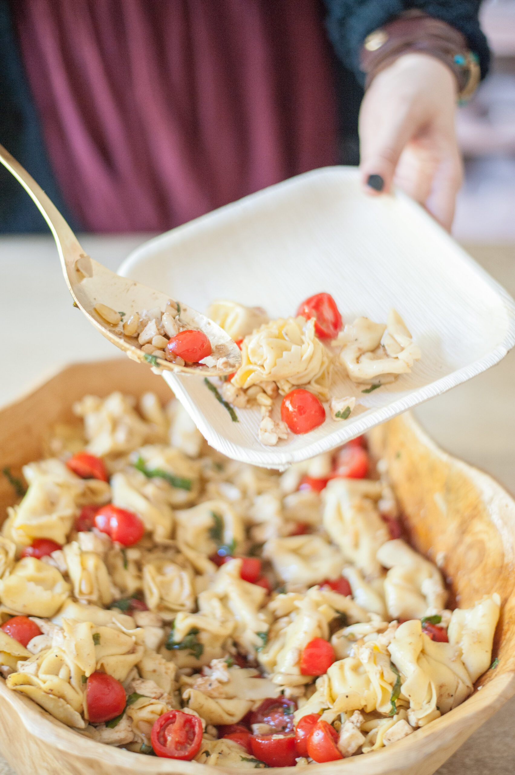 woman putting a Caprese Tortellini Salad on a white plate