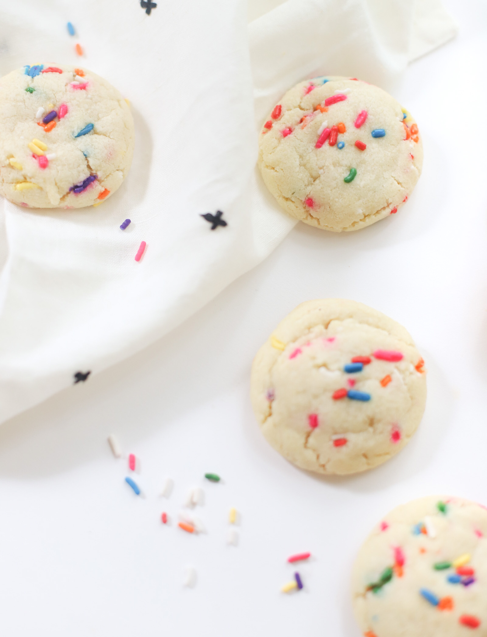 four pieces of Dairy Free Sprinkle Sugar Cookies with sprinkles on top of a white cloth