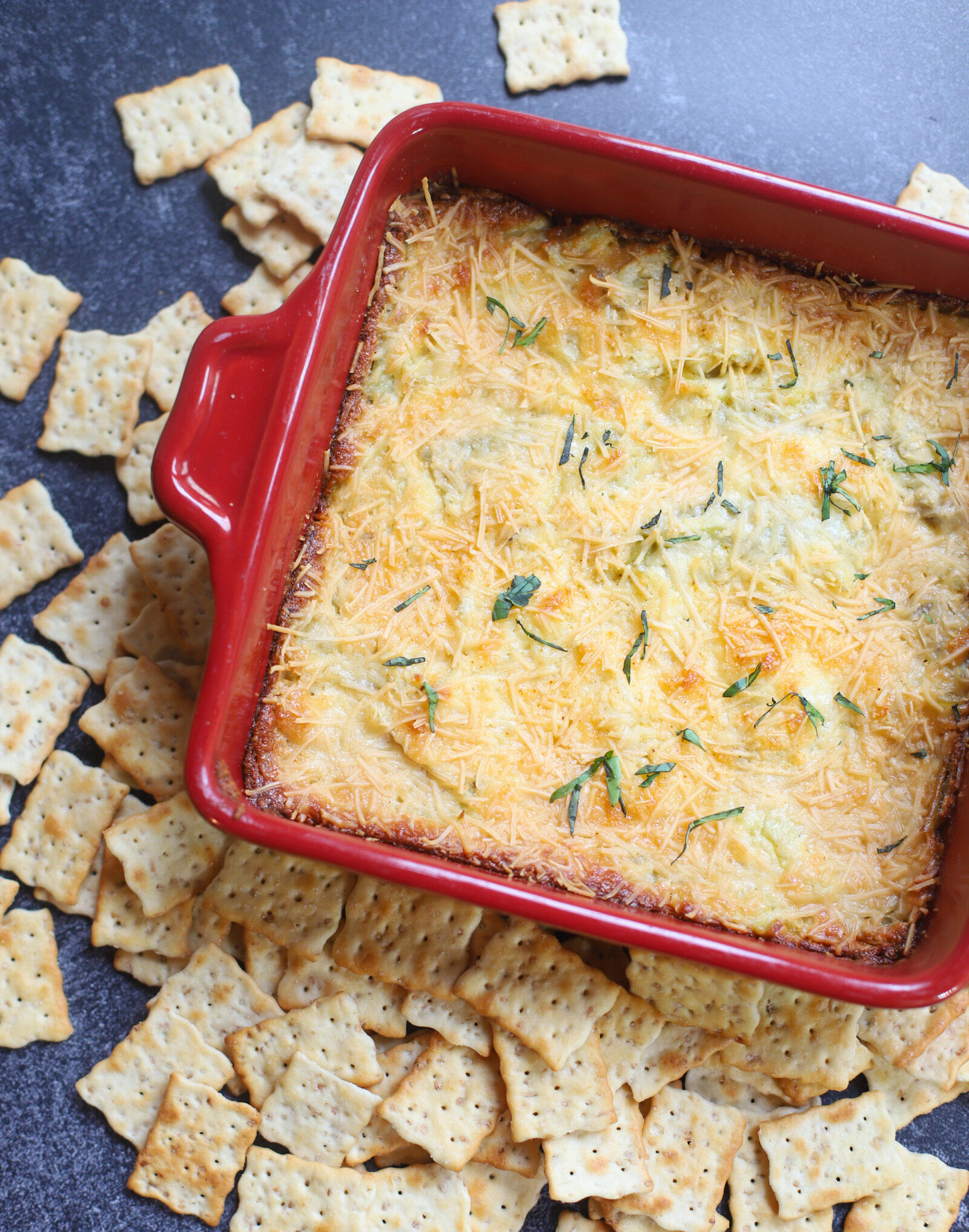 The Best Ever Easy Baked Artichoke Dip on a red baking pan 